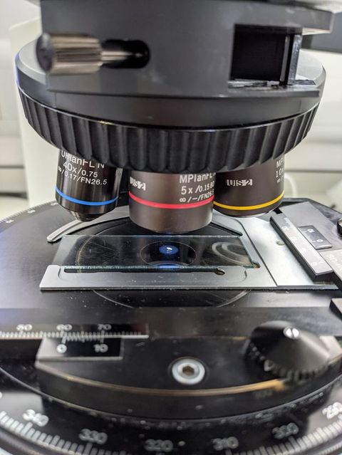 A microscope seen face-on, with a slide resting on it.