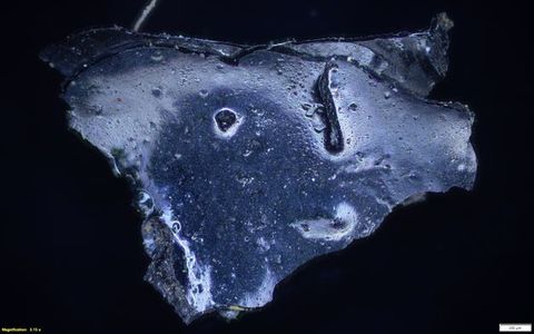 Colour photograph. Magnified photograph of a rock or mineral in a vibrant shade of blue, showing a close-up view of its surface and texture against a black backdrop. On the lower left yellow text reads, ‘Magnification: 3.15 x’. On the right, a small white rectangle bears the number 200.