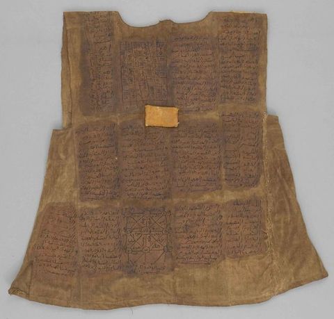 Colour photograph. A close-up section of pale brown fabric decorated with a series of highly detailed geometric and organic black patterns drawn into squares, and arranged into a grid formation divided by intersecting lines.